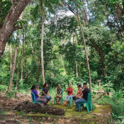 Group of 7 people are sitting around a circle in a forest.